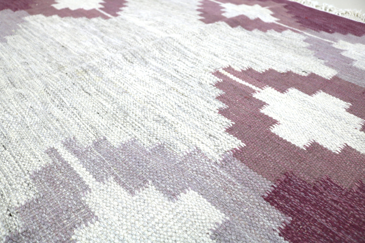 Close-up of Swedish Kilim rug with burgundy and ivory geometric motifs and woven texture
