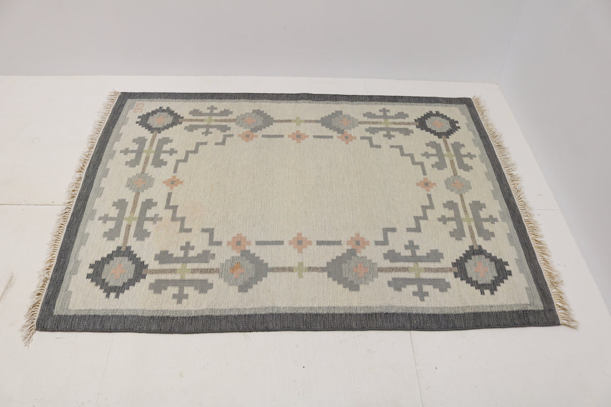 Angled view of Swedish Kilim rug featuring ivory field, grey border and geometric motifs