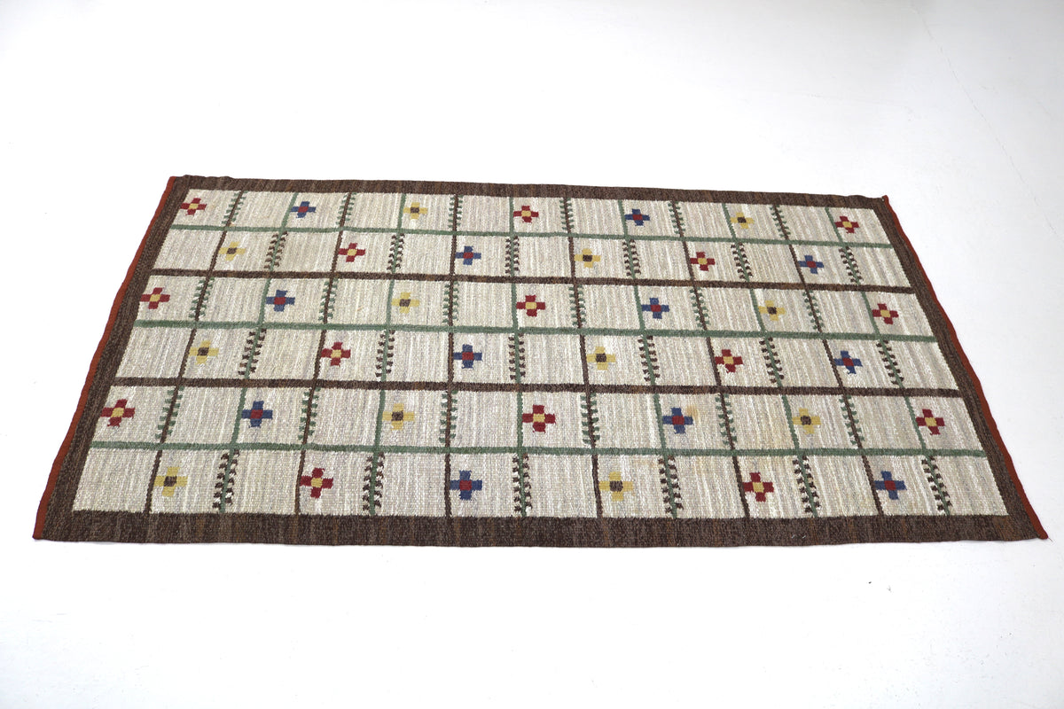 Angled view of Swedish Kilim rug featuring ivory panels and multicoloured geometric motifs