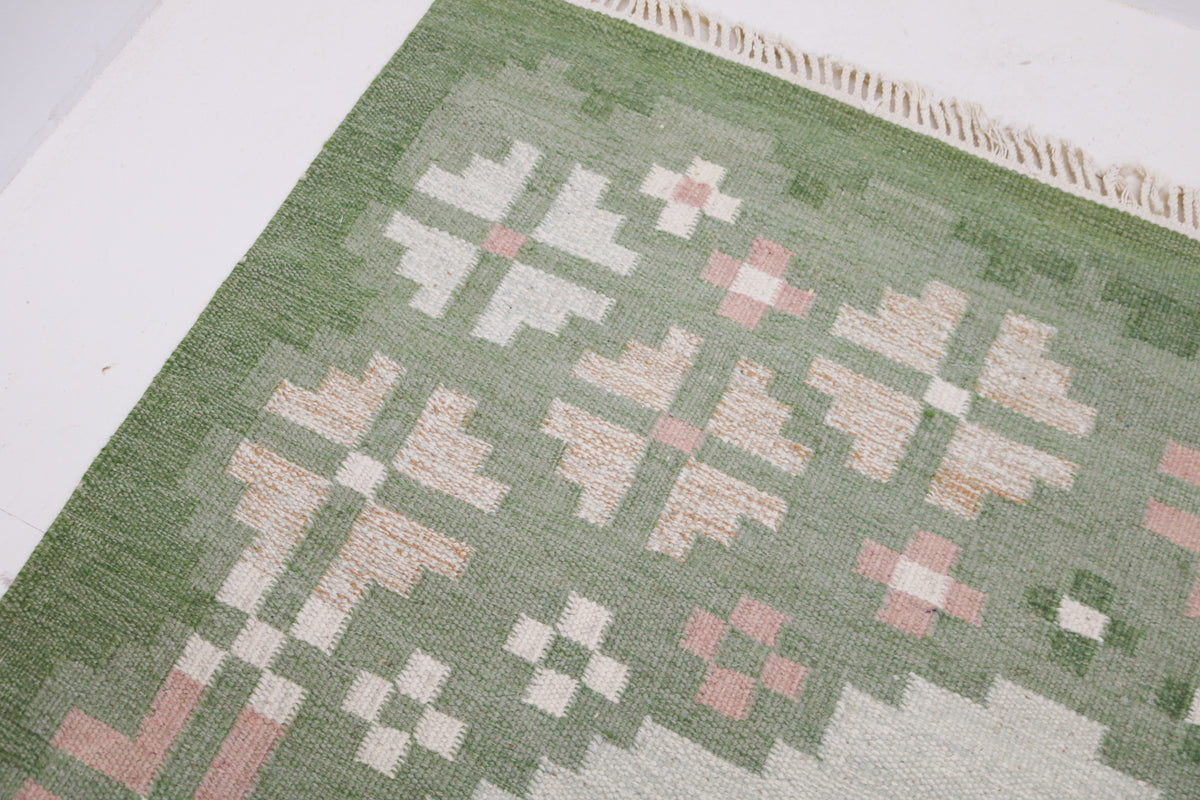 Close-up of Kilim rug border with geometric floral patterns in sage green and muted pink