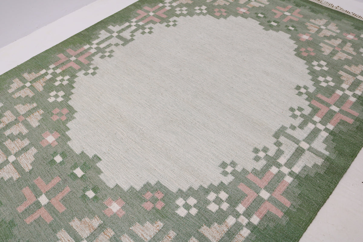Close-up of vintage Kilim rug featuring geometric floral motifs in green, ivory and pink