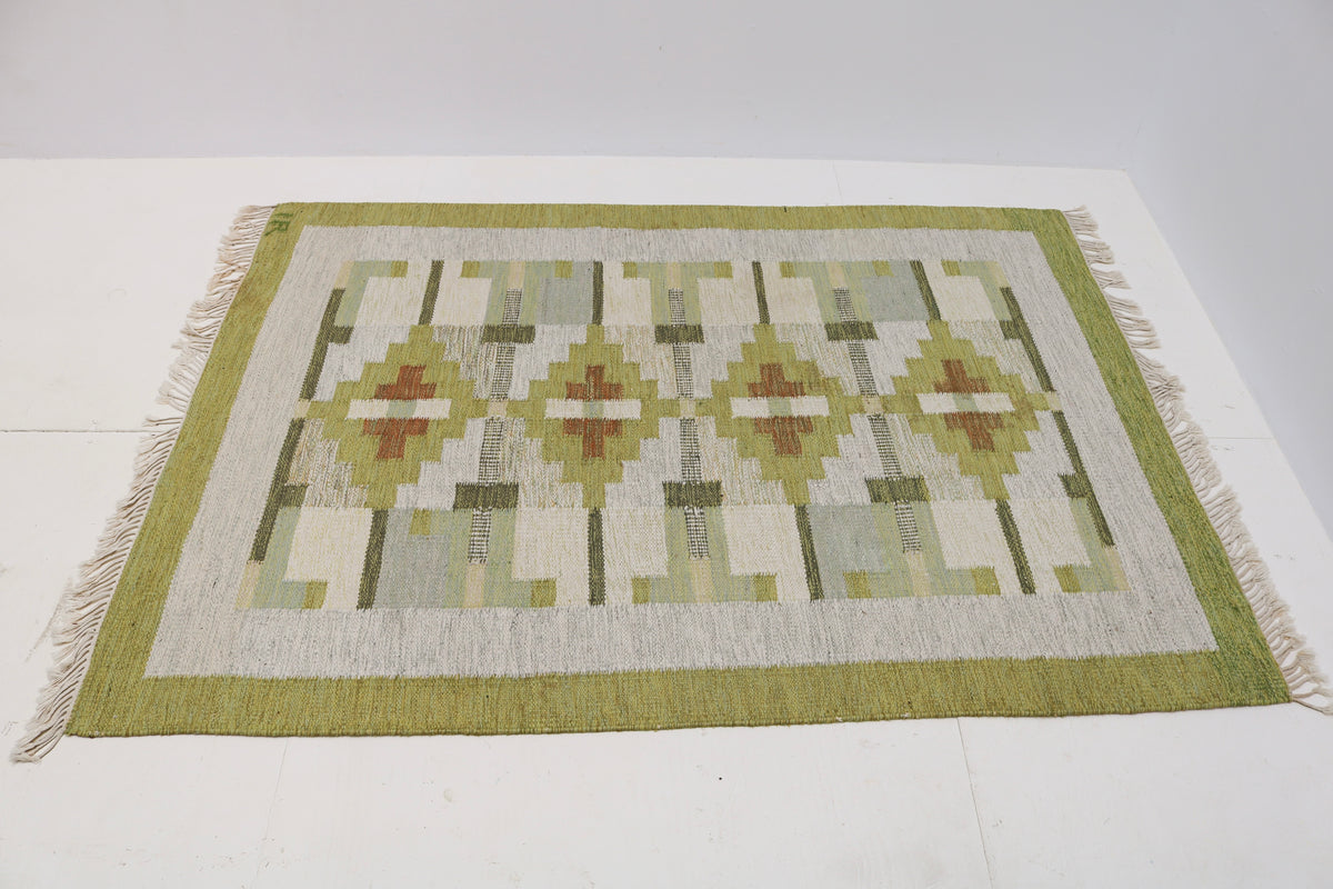 Angled view of Swedish Kilim rug featuring olive, sage, ivory and pale blue-grey motifs