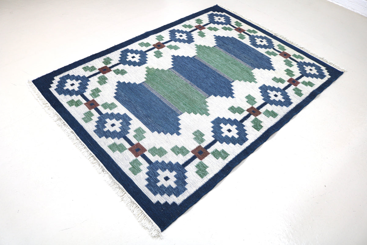 Angled view of Swedish Kilim rug featuring blue and green geometric blocks with floral motifs
