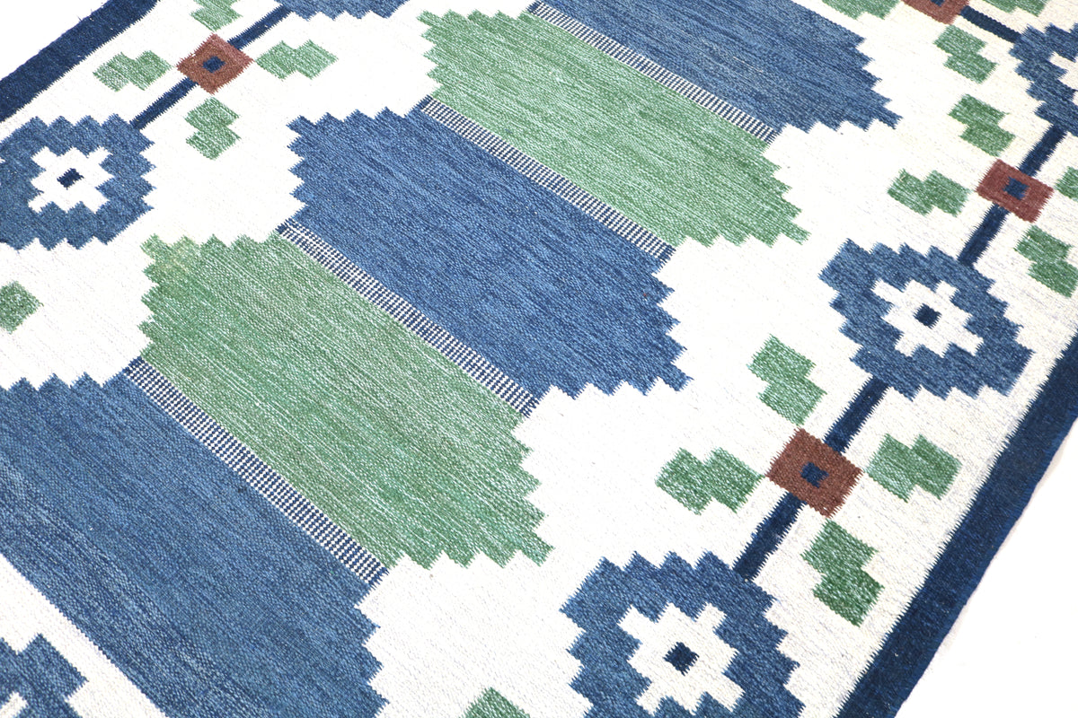 Close-up of Swedish Kilim rug corner with geometric floral motifs and contrasting blue border
