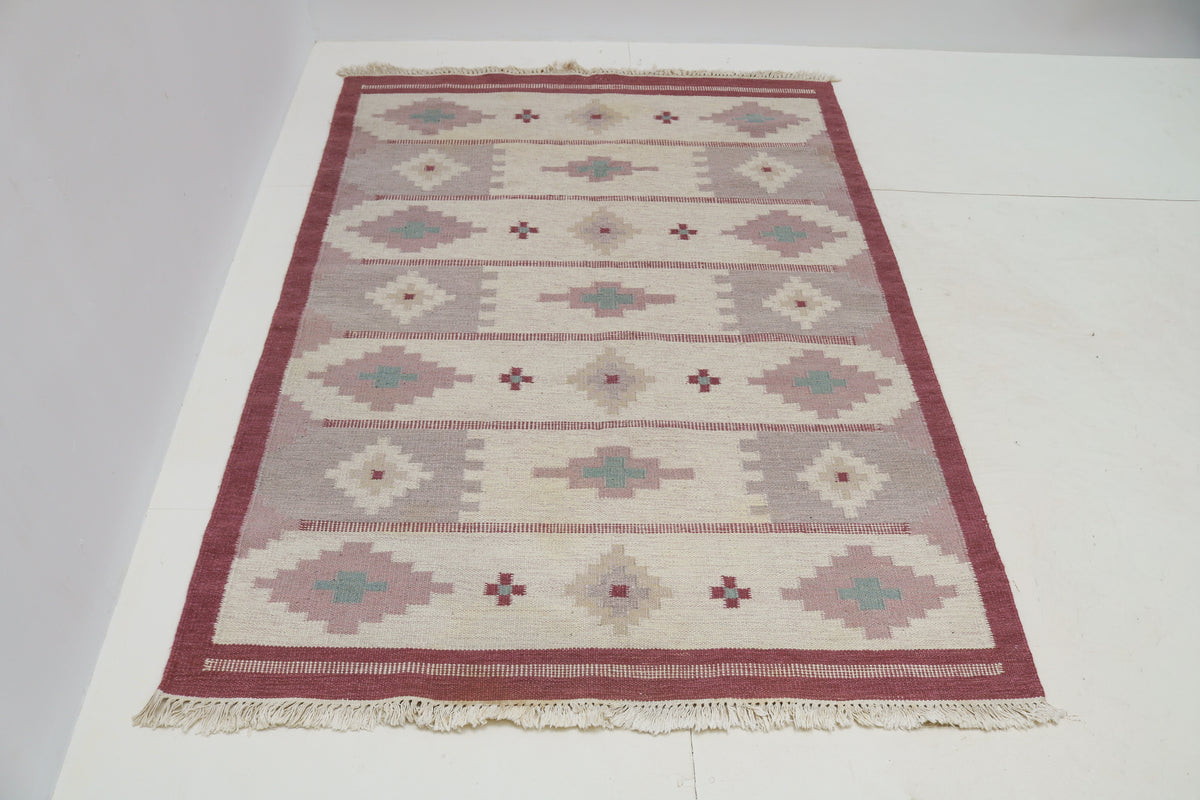 Angled view of Swedish Kilim rug featuring muted pink, cream and blue-green patterns