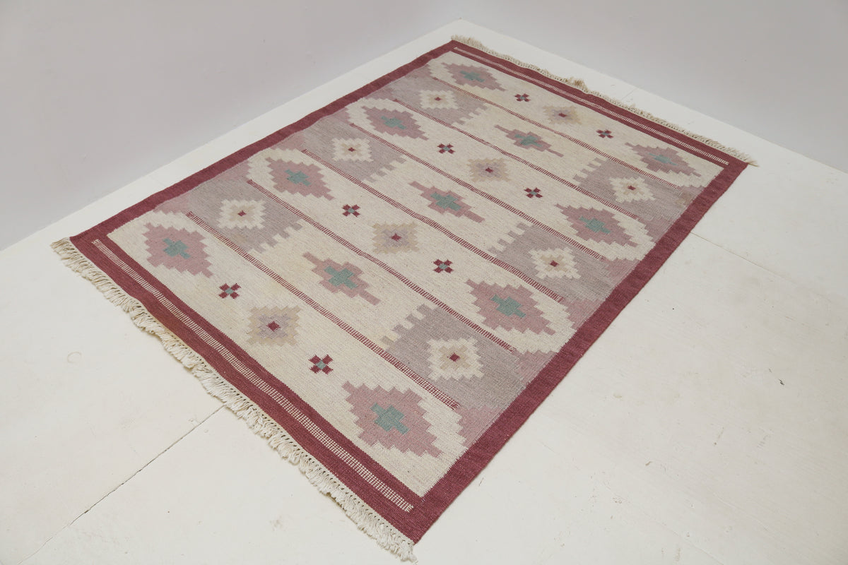 Angled view of Kilim rug with dusty pink border and repeating geometric motifs