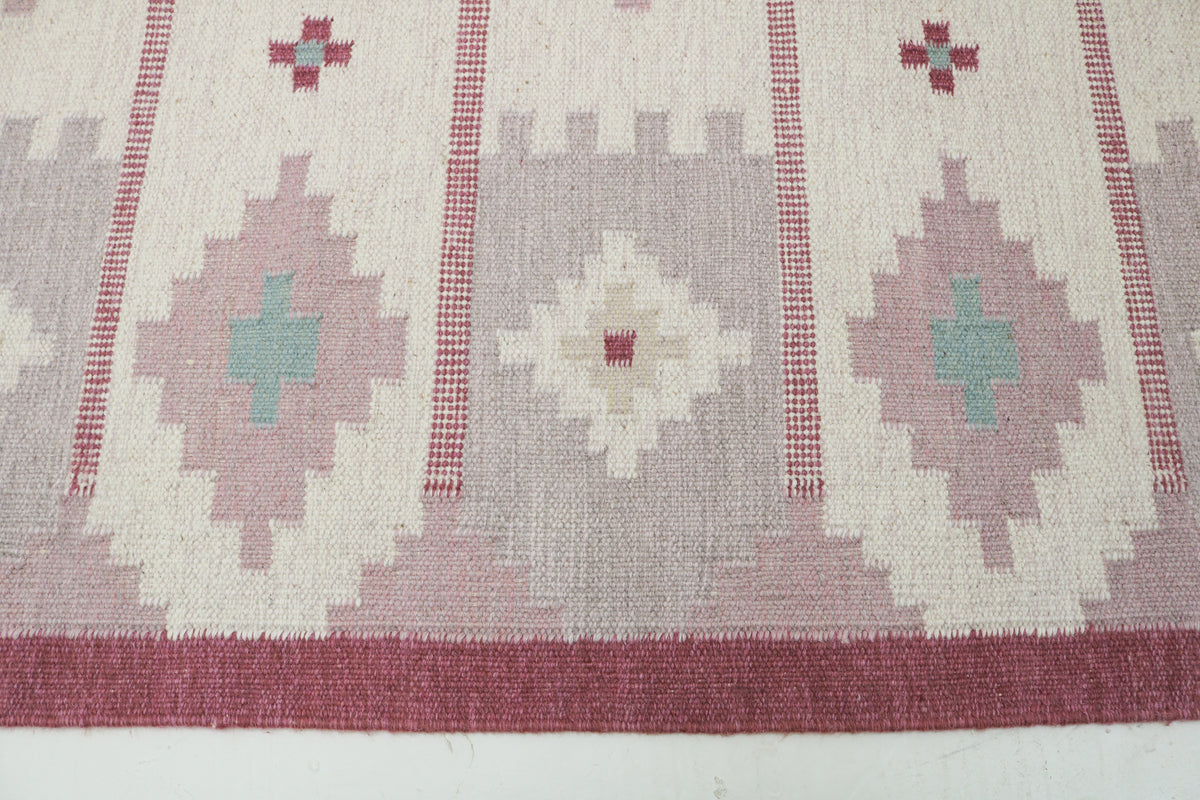 Close-up of vintage Swedish rug showing repeating geometric motifs in muted pink and cream