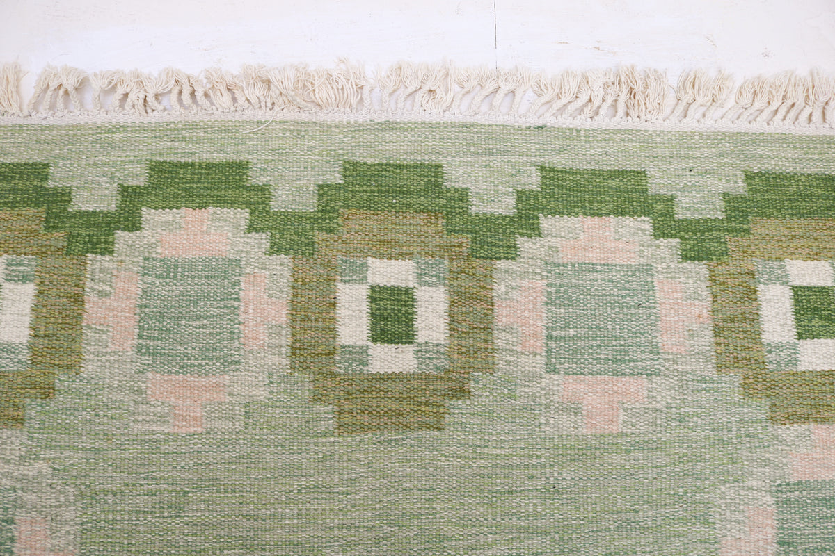 Close-up of vintage Kilim rug featuring geometric motifs in green, ivory and pale pink
