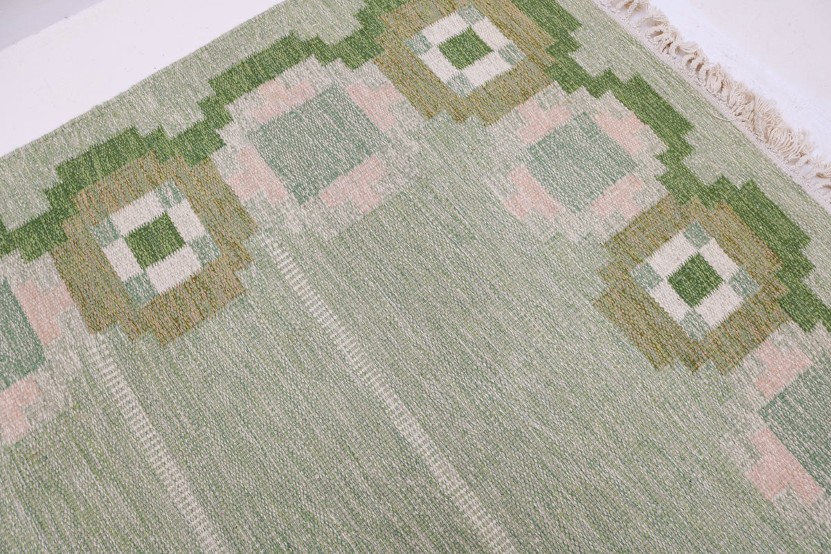 Detailed view of Swedish Kilim rug with geometric border surrounding the soft green field
