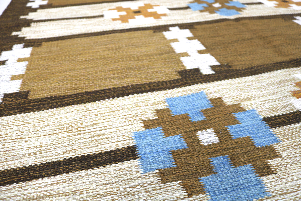 Close-up of Kilim rug with blue and ochre geometric motifs against an earthy brown field