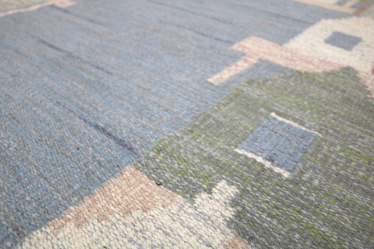 Close-up of Swedish Kilim rug with abstract houses, trees and soft blue hills