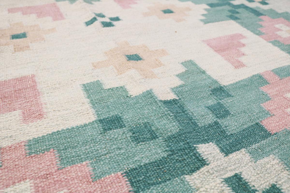 Close-up of vintage Kilim rug showing repeating floral motifs in soft green and pink