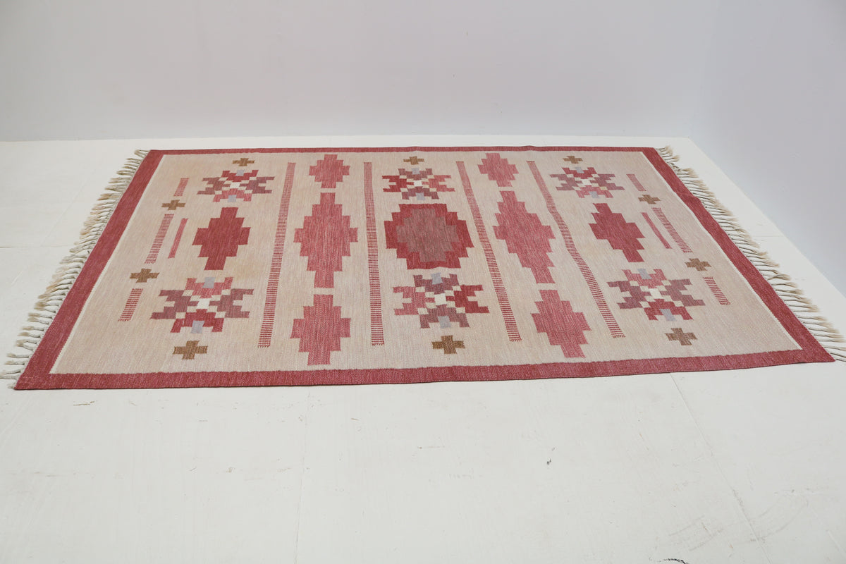 Angled view of Swedish Kilim rug featuring dusty rose, ivory and muted red geometric patterns