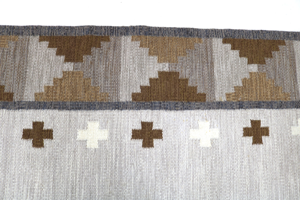 Close-up of Kilim rug with brown and ivory geometric motifs on a soft grey field
