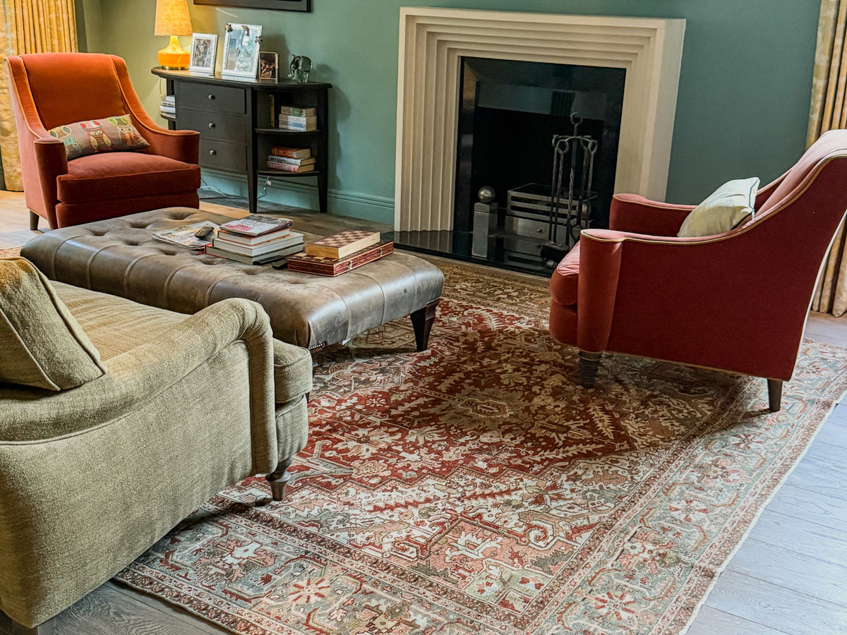 Antique Persian Heriz rug in a sage-green sitting room with velvet armchairs and a leather ottoman