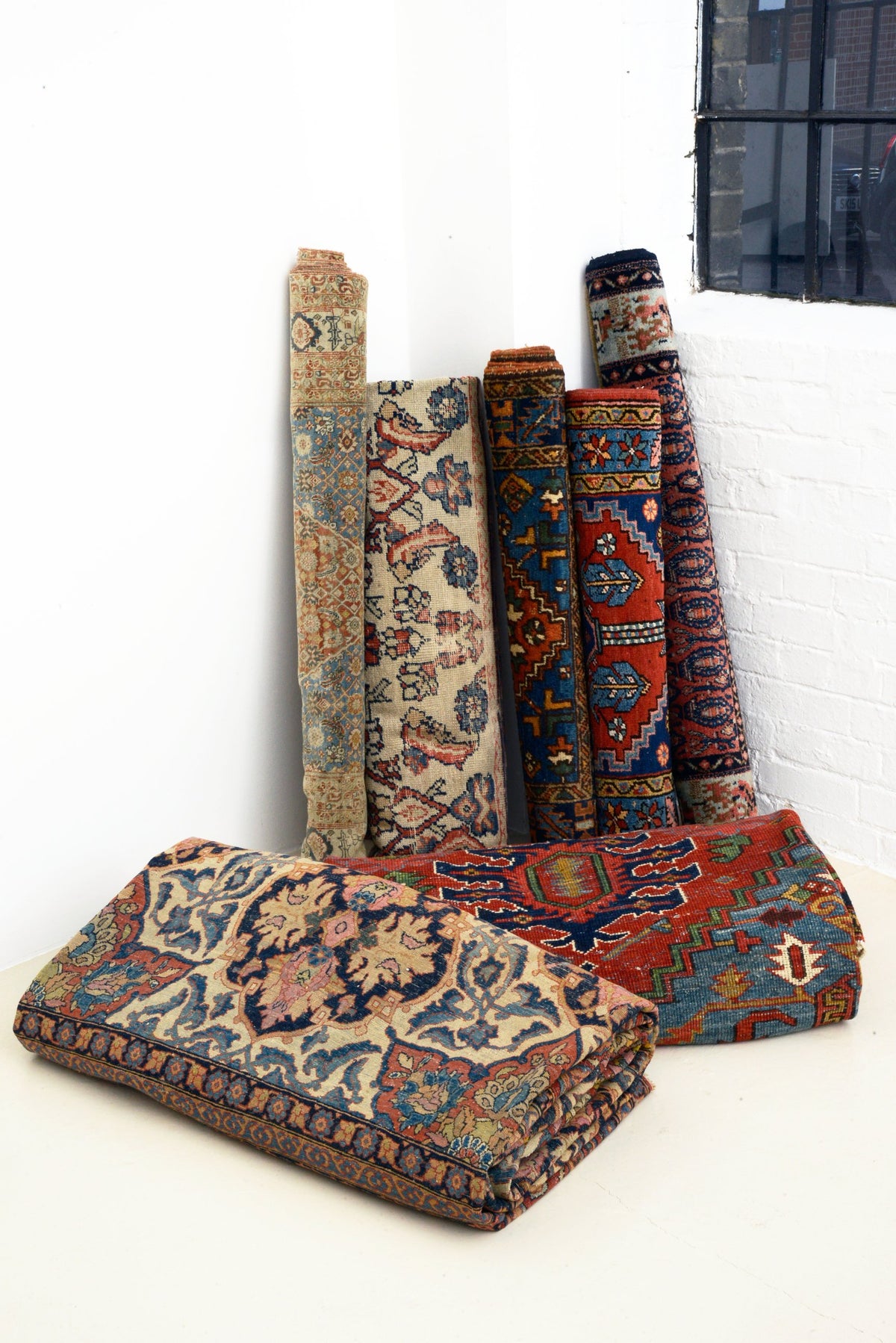 Antique Persian rugs rolled and folded in the Hakiemie Rug Gallery stockroom